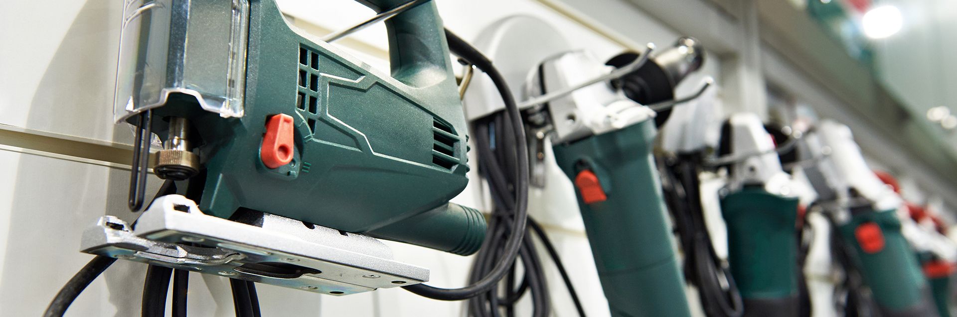 Eine Reihe von verschiedenen Elektrowerkzeugen, darunter Sägen und Bohrer, ordentlich an einer Ausstellungswand in einem Baumarkt angeordnet.